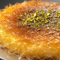 Delicious kunafa topped with crushed pistachios served on a white plate during a festive gathering photo