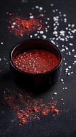 A bowl of savory spice mix is surrounded by scattered salt on a dark background for culinary inspiration photo