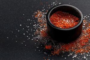 Spicy seasoning blend in a black bowl on a dark surface with contrasting salt granules surrounding it photo