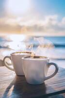 Two steaming cups of coffee by the ocean at sunrise photo