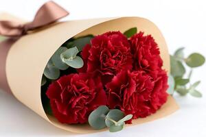 Bouquet of red carnations wrapped in brown paper tied with a ribbon is lying on a white background photo