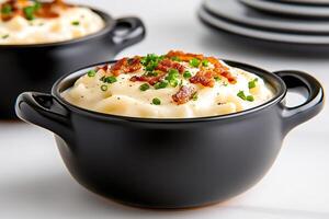 Creamy mashed potatoes with bacon and chives topping in black ceramic bowl photo