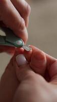 Mom's hands hold the tiny baby foot and using the little scissors to cut the toenails. Taking care of a child. Close up. Blurred backdrop. Vertical video