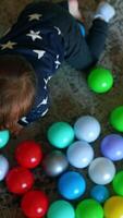 Happy Caucasian toddler crawls by the floor with lots of balls around. Baby picks one ball and pulls it into his mouth. Top view. Vertical video