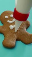 Hand of human is decorating by white glaze gingerbread biscuit with using brush bits on a turquoise background for Christmas. Close-up Vertical video
