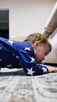Funny little kid wants to get something from under the sofa. Boy shoves his hand under the furniture but can't get what he wants. Vertical video