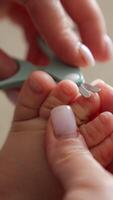 Caring about the child. Mom's hands hold the tiny toes and cut the toenails with scissors. Close up. Blurred backdrop. Vertical video