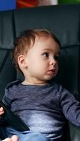 Serious little toddler sitting in a black leather chair. Beautiful child turning remote control in hands and pressing buttons. Vertical video