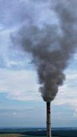 View from the drone at the old aged weathered tall industrial factory chimney with smoke over it. Cloudy sky background. Vertical video