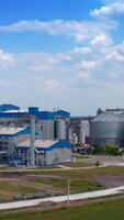 Modern plant on field. Metal silos with grain. Grain storage tank on green nature background. Grain storage on large factory. Aerial view. Vertical video