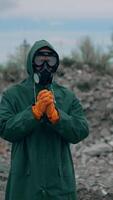 Virologist man in protective costume and respirator gas mask standing in a deserted city at the industrial factory and a lot of trash background. Vertical video