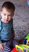 Cute Caucasian toddler playing with toys on the floor. Kid presses button on the toy and watches it working. Top view. Vertical video