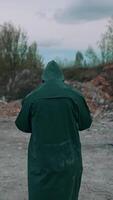 Virologist man in protective costume and respirator gas mask walking near landfill site pollution and looking at the scale of the disaster. Ecological disaster concept. Vertical video
