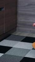 Beautiful toddler in orange clothes sits on the kitchen floor. Baby crawls up to the closet trying to open the door. Vertical video