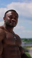 Waist up portrait view of the strong stylish man wearing glasses while posing on clear blue sky background. Shirtless bodybuilder showing his muscles. Vertical video