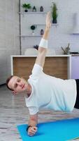 Young man is training at home. Man doing exercise on a mat on kitchen background. Guy working hard to maintain body shape during isolation.. Vertical video