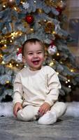 Amazing lovely little toddler laughing happily and then crawling up to camera. Decorated Christmas tree at backdrop. Vertical video