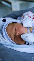 Sweet tiny infant in cap and mittens sleeping. Tiny newborn baby boy in blankets on bed. Close up. Vertical video