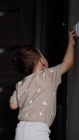 Curious one year old toddler playing with the light switch. Rear view of a little boy turning the light on and off in the room. Vertical video