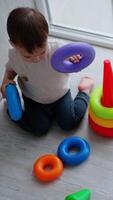 Adorable Caucasian toddler sits on his knees on the floor. Child constructs the pyramid on the balcony. View from top. Vertical video