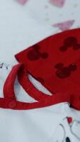 Red cap and white bodysuit with letters on the table. Pieces of clothes for a newborn child. Close up. Vertical video