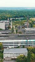 Large industrial territory on nature background. Many buildings of abandoned factory in the countryside. View from above.. Vertical video