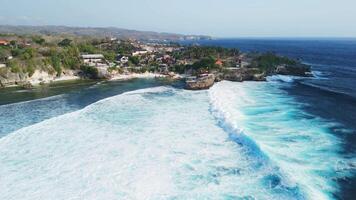 Coastline with rocks, sandy beach and ocean waves on Nusa Ceningan island. Drone view video