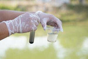 Close up scientist hand hold glass tube that contains sample of water to do science experiment. Concept Testing of water quality and contaminants from natural water sources photo