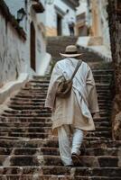 A man in white clothes and a hat walks up some stairs photo