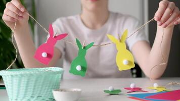 Boy made Easter paper garland. Multicolored Easter bunnies made of paper and pompons on string with clothespins video
