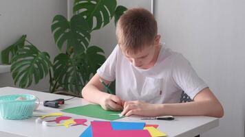 Blond Boy is sitting at the table and diligently making an Easter decoration garland. Hands trace outline of Easter bunny on paper video