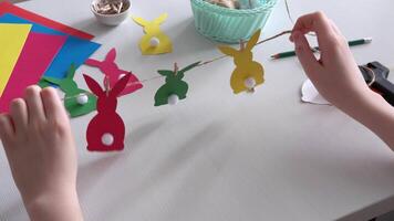 Boy made Easter paper garland. Multicolored Easter bunnies made of paper and pompons on string with clothespins video