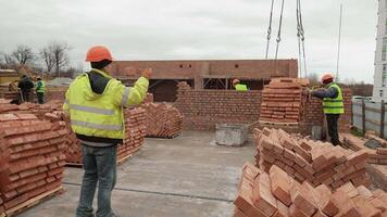 Construction workers unloading bricks on site, A group of construction workers in safety gear unloading a pallet of bricks on a building site. video