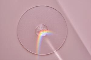 A drop of serum on a round stand on a pink background with beautiful caustics. photo