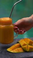 de cerca Disparo de un vaso de un mango sacudir y cortar mangos en un lado de un nadando piscina con un inoxidable Bebiendo Paja en eso alternativa a el plastico Bebiendo pajitas eco simpático productos nutrición video