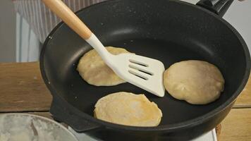 Raw pancakes are flipped over in a pan using a spatula to ensure even cooking on all sides. high angle video