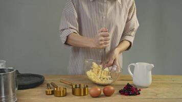 Young woman is crushing bananas in bowl, turning them into pulp that will be used as mashed potatoes for pie. She is also preparing berries and other fruits to use in pie. video