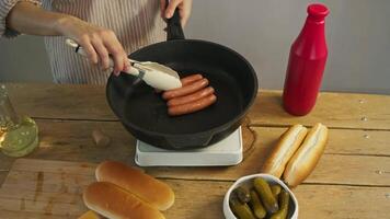 The chef makes sure that the sausages, prepared from meat, do not become overcooked by turning them over while they are being fried in a pan, using tongs. video