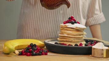Traditional American breakfast consists of stack of pancakes topped with fresh berries and powdered sugar, which are then drizzled with generous helping of delicious red sweet jam. video