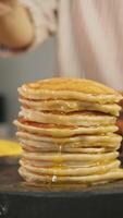 Significant amount of maple syrup or honey drips from spoon onto plate on which there are freshly prepared delicious pancakes. Vertical. video