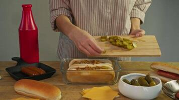 In the rustic-style kitchen, the chef prepares a classic hot dog and puts slices of pickled cucumber between freshly baked buns. video