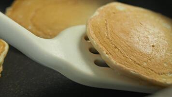 A freshly made pancake is carefully lifted from the hot pan with a spatula and placed on top of a stack with the other pancakes. Close up video