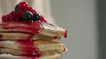 There are several different types of berries on top of stack of freshly prepared delicious donuts for breakfast, and sweet red jam drips from the edge of pancake. video
