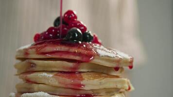 A delicious red, sweet and sugary jam made from fresh berries flows along the edge of a stack of fluffy American pancakes. Close up video