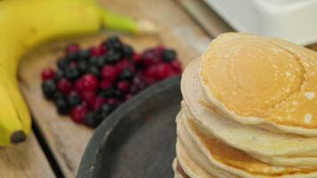 Close-up of stack of fresh pancakes, stacked on top of each other. They are served for breakfast, along with variety of red berries and a banana. video