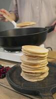 The freshly cooked pancake is carefully lifted from the hot pan using a spatula and placed on top of a stack of other pancakes. Vertical. video