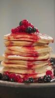 Variety of berries adorn top of a stack of freshly baked, delectable donuts, while a sweet, red jam oozes from the edge of a pancake. Vertical. video