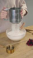 Chef sifts wheat flour through sieve and then adds it to bowl, preparing dough for either blueberry pie or pancakes with berries. video