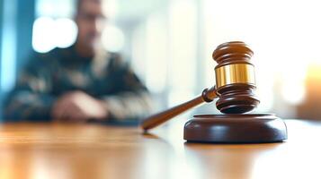 A gavel rests on a wooden table, symbolizing law and justice, while a person sits in the background during court proceedings. photo