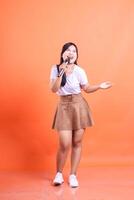 Portrait of a woman singing into a microphone during a performance, the stage is all hers. isolated on orange background photo